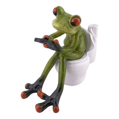 Eine Dekofigur vor weißem Hintergrund, die einen Frosch auf Toilette abbildet. Der Deko Frosch ist einer ganz alltäglichen Situation mit seinem Smartphone in der Hand dargestellt.