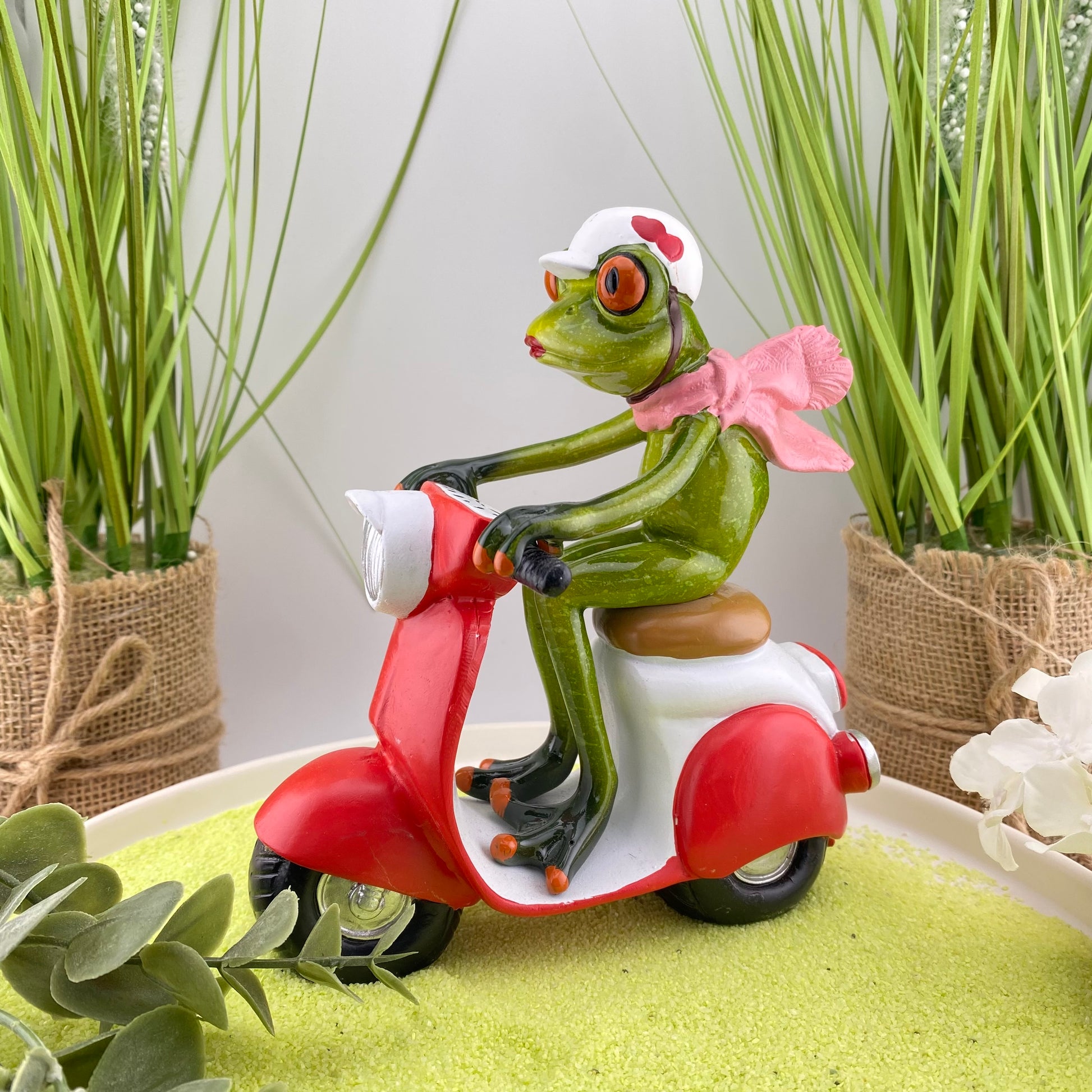 Eine Dekofigur im Ambiente, die einen weiblichen Frosch auf einem rotem Roller abbildet.