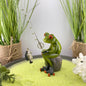 Eine Dekofigur im Ambiente, die einen Frosch Mann beim Angeln abbildet. Der Deko Frosch sitzt gemütlich und schaut seinen geangeleten Fisch am Haken seiner Angel an.