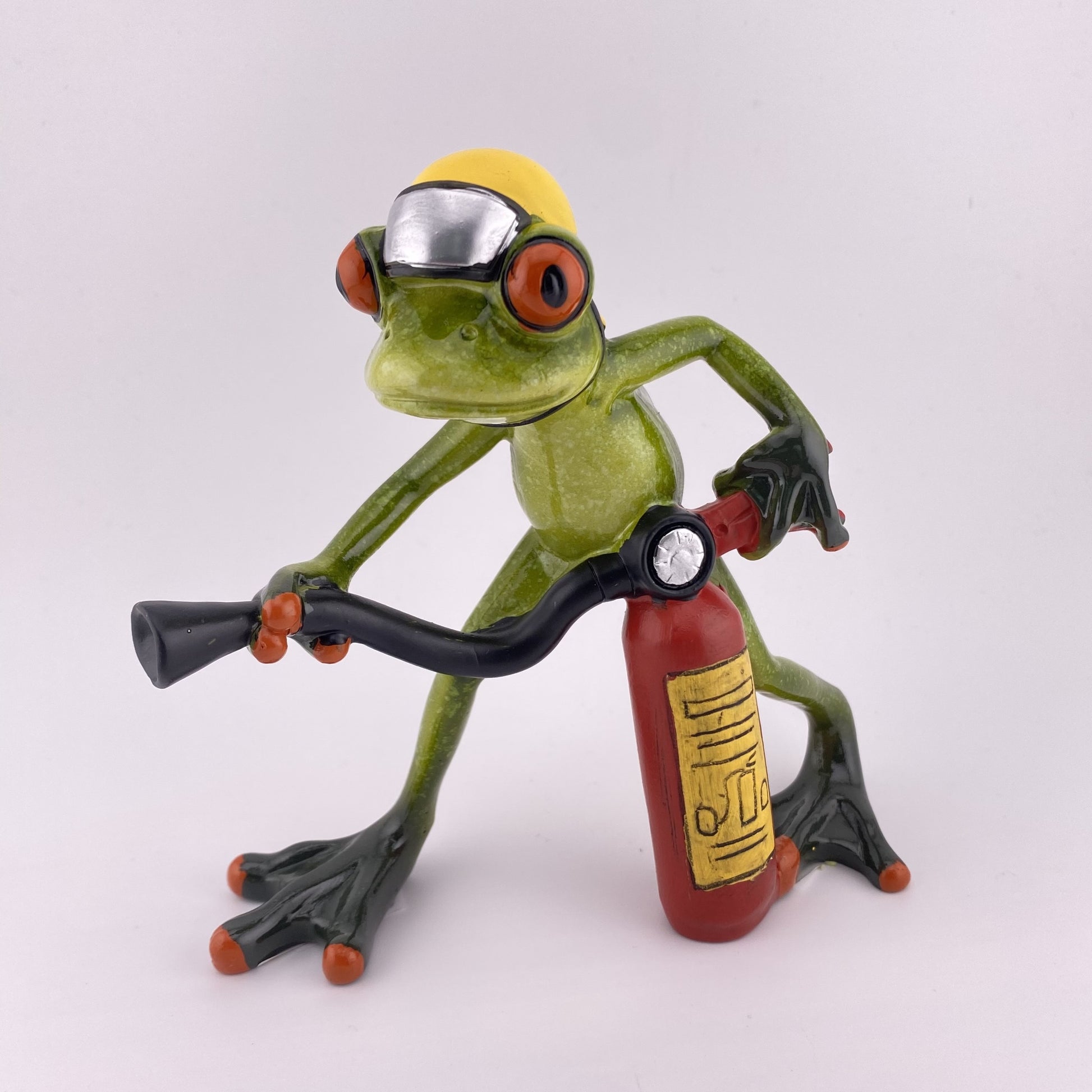 Eine Dekofigur vor weißem Hintergrund, die einen Frosch Feuerwehrmann mit Feuerlöscher in den Händen und Feuerwehrhelm abbildet.