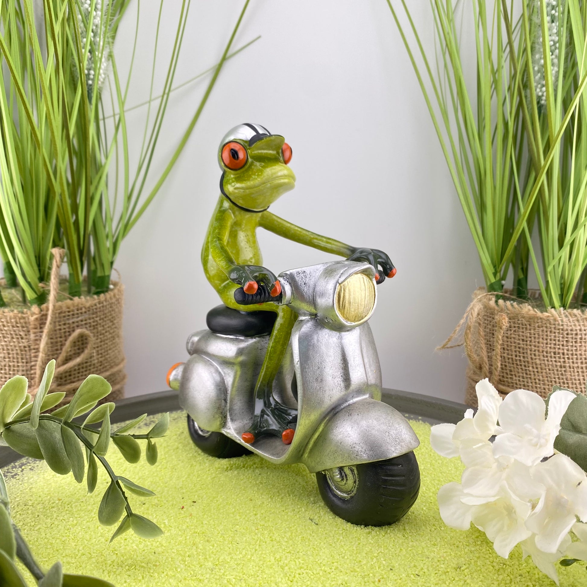 Eine Dekofigur im Ambiente, die einen männlichen Frosch auf einem silbernen Roller abbildet.
