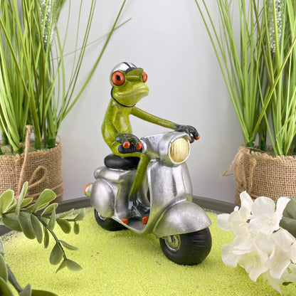 Eine Dekofigur im Ambiente, die einen männlichen Frosch auf einem silbernen Roller abbildet.