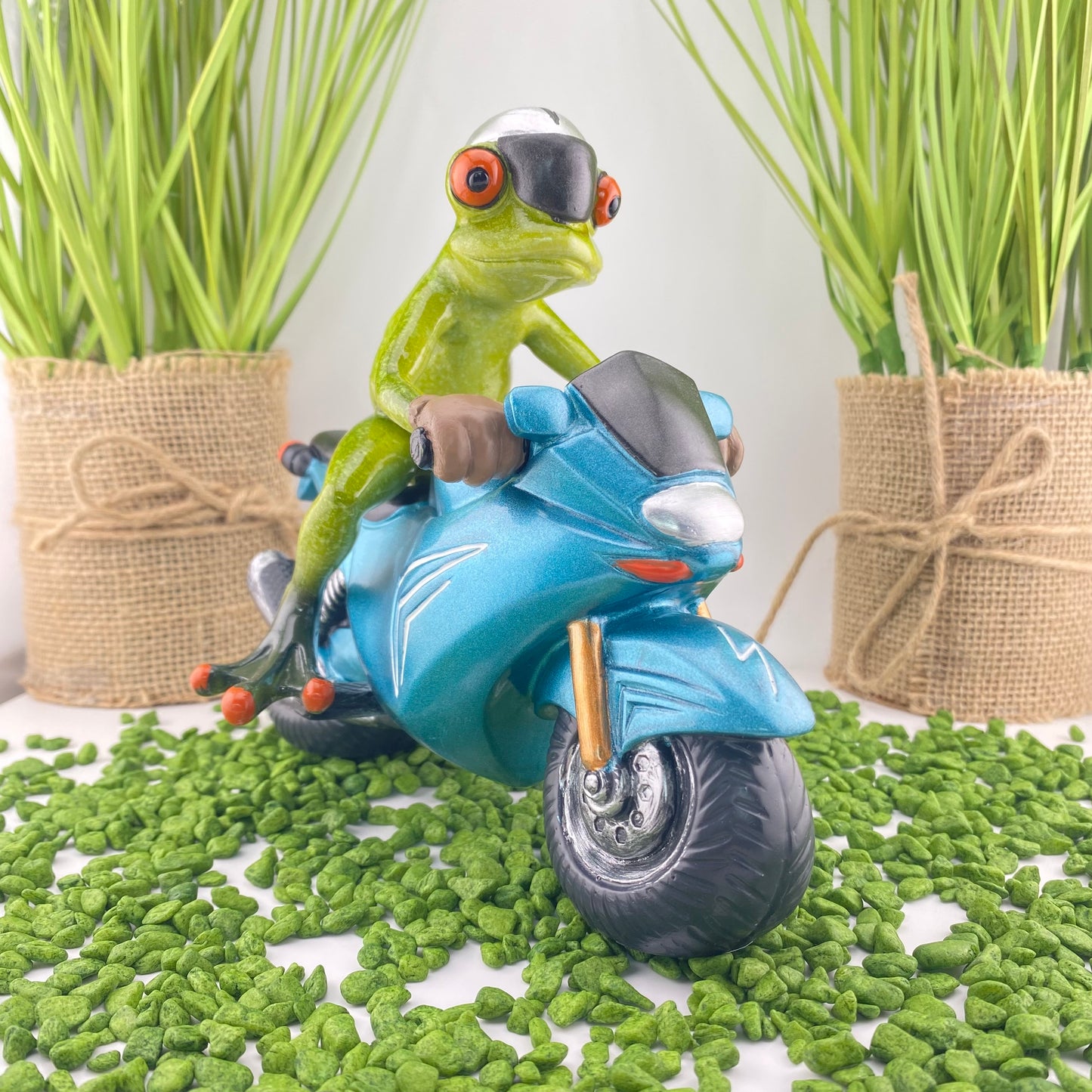 Ein Dekofigur Frosch der Serie Froschhausen sitzt auf einem blauen Motorrad und ist im Ambiente platziert.