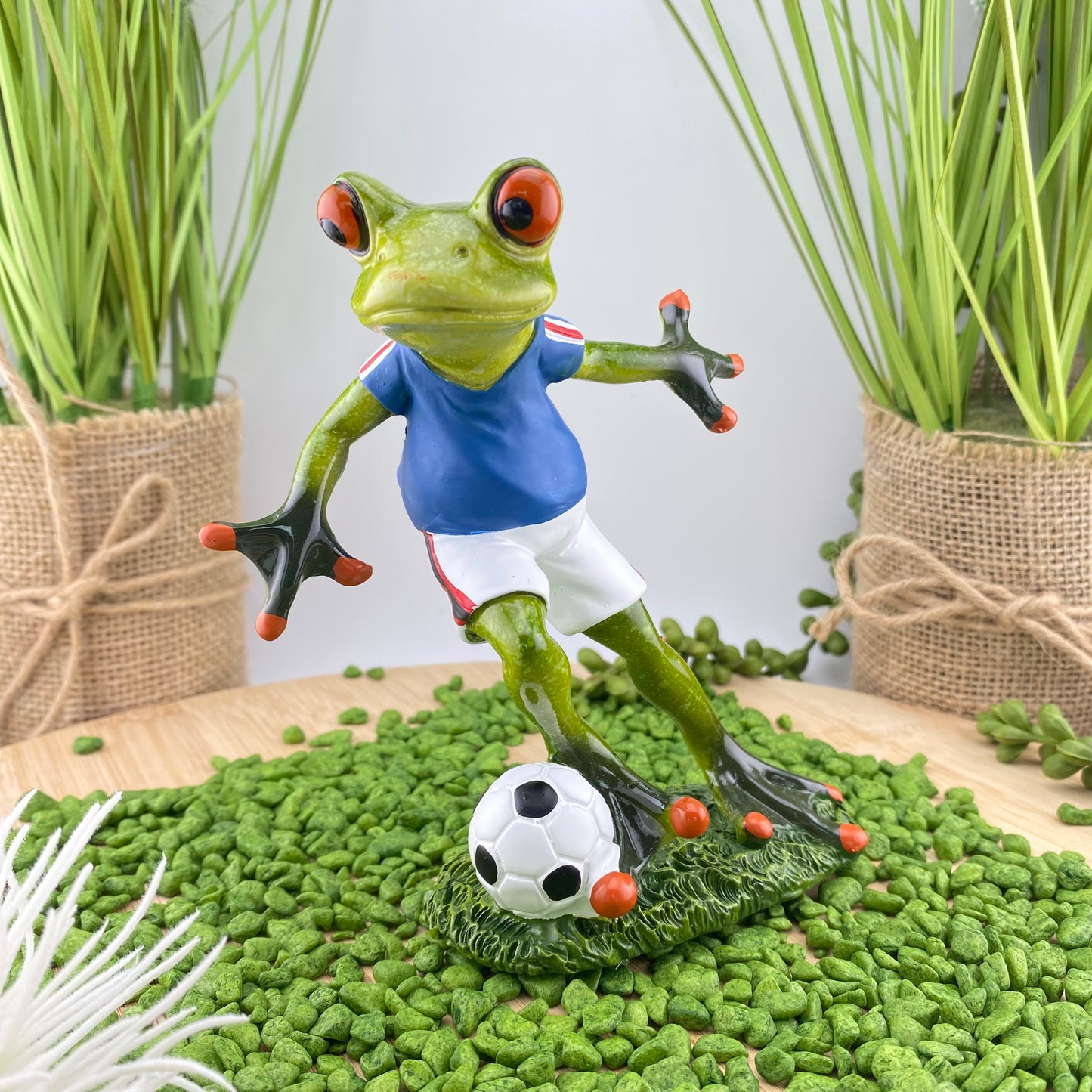 Eine Dekofigur im Ambiente, die einen fußballspielenden Frosch in blauem Trikot mit Fußball abbildet.