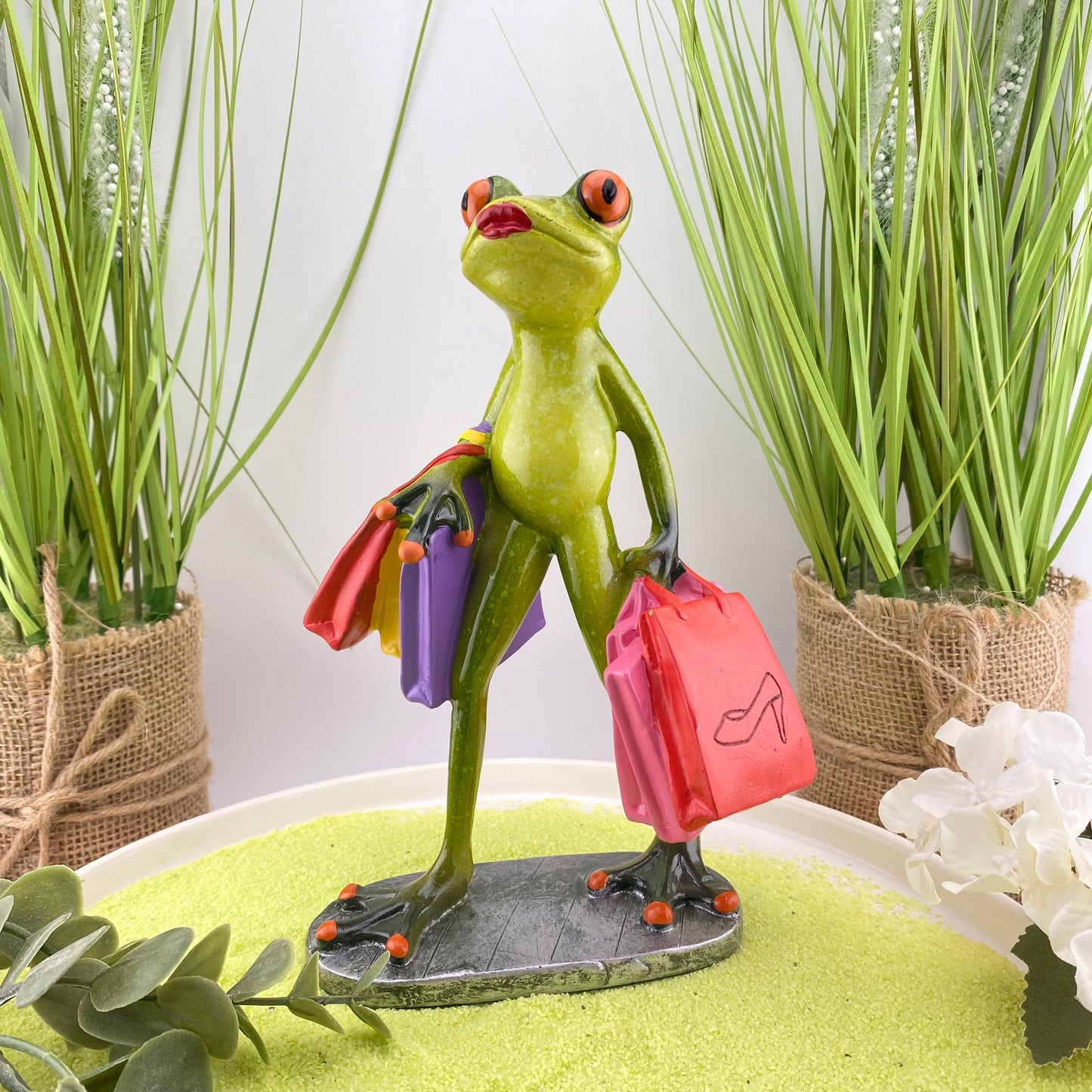 Eine Dekofigur im Ambiente, die einen  weiblichen Frosch mit Einkaufstüten abbildet. Die Frosch Lady ist gerade am shoppen.Eine Einkaufstüte trägt den Schriftzug "Ladies Day". 