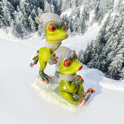 Dekofroschpaar Ski und Schlitten fahrend mit Schal und Mütze im Ambiente platziert