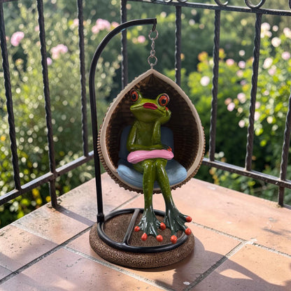 Grüner Formano Frosch mit rosa Kissen in einem hängenden Eiersessel vor einem grünen Garten.