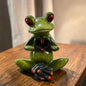 Sitzender grüner Formano Frosch formt mit seinen dunklen Händen ein Herz auf einem hellbraunen Holztisch.