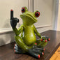 Sitzender grüner Formano Frosch zeigt einen erhobenen Mittelfinger auf einem dunklen Holzregal vor einer hellen Wand.