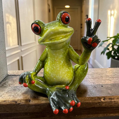 Sitzender grüner Formano Frosch zeigt mit einer Hand ein Peace-Zeichen auf einem rustikalen Holzregal.