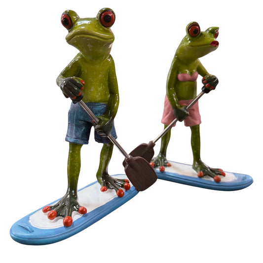 Zwei grüne Formano Frösche in blauer Badehose und rosa Bikini stehen mit Paddeln auf blau-weißen Paddleboards vor weißem Hintergrund.