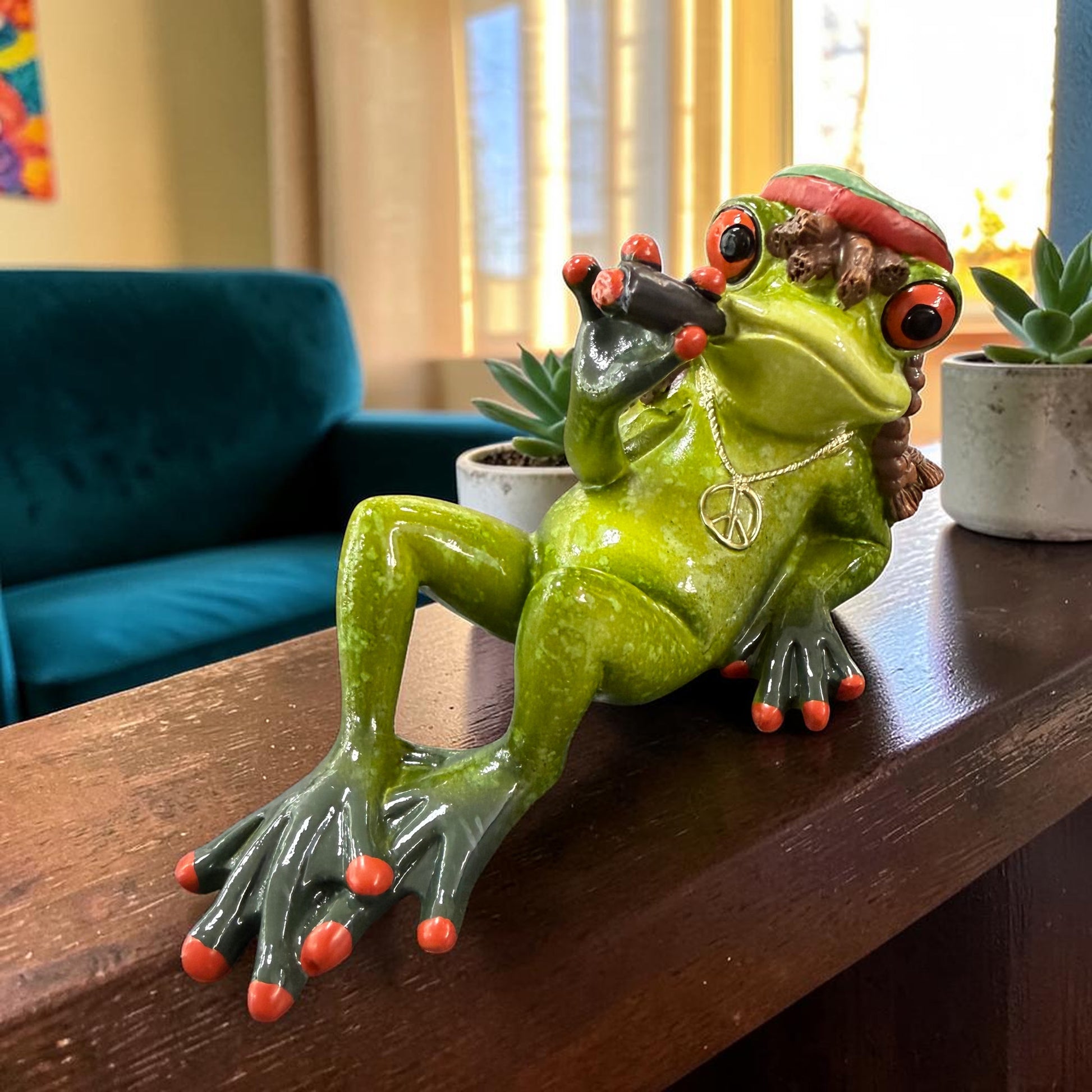 Grüner Formano Hippie-Frosch mit roter Mütze, Peace-Kette und Zigarre liegt auf einer dunklen Holzfläche.