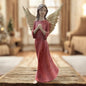 Eine Deko-Engelfigur mit goldfarbenen Flügeln und rotem Kleid mit Hand anm Herz im Ambiente
