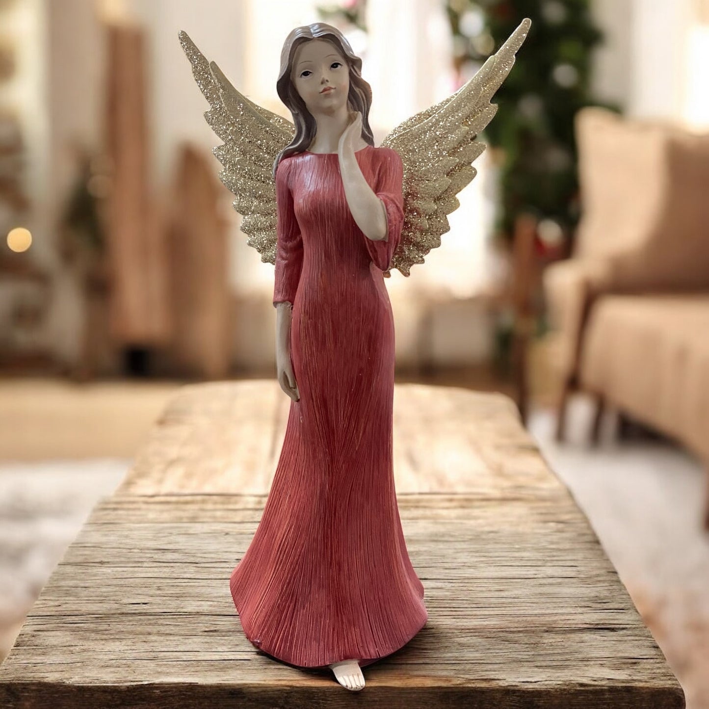 Eine Deko-Engelfigur mit goldfarbenen Flügeln und rotem Kleid mit Hand an Hals im Ambiente