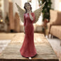 Eine Deko-Engelfigur mit goldfarbenen Flügeln und rotem Kleid mit Hand an Hals im Ambiente