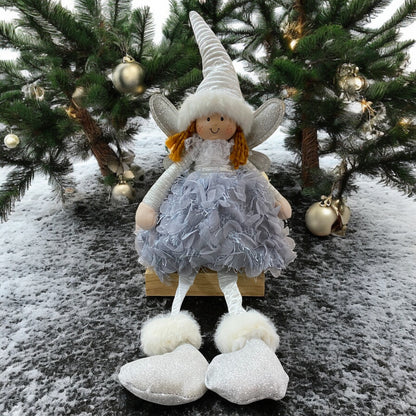 Eine sitzende Stoff-Engelfigur mit langer Zipfelmütze, silbernen Flügeln und flauschigem Kleid in der Farbe Blau im Ambiente