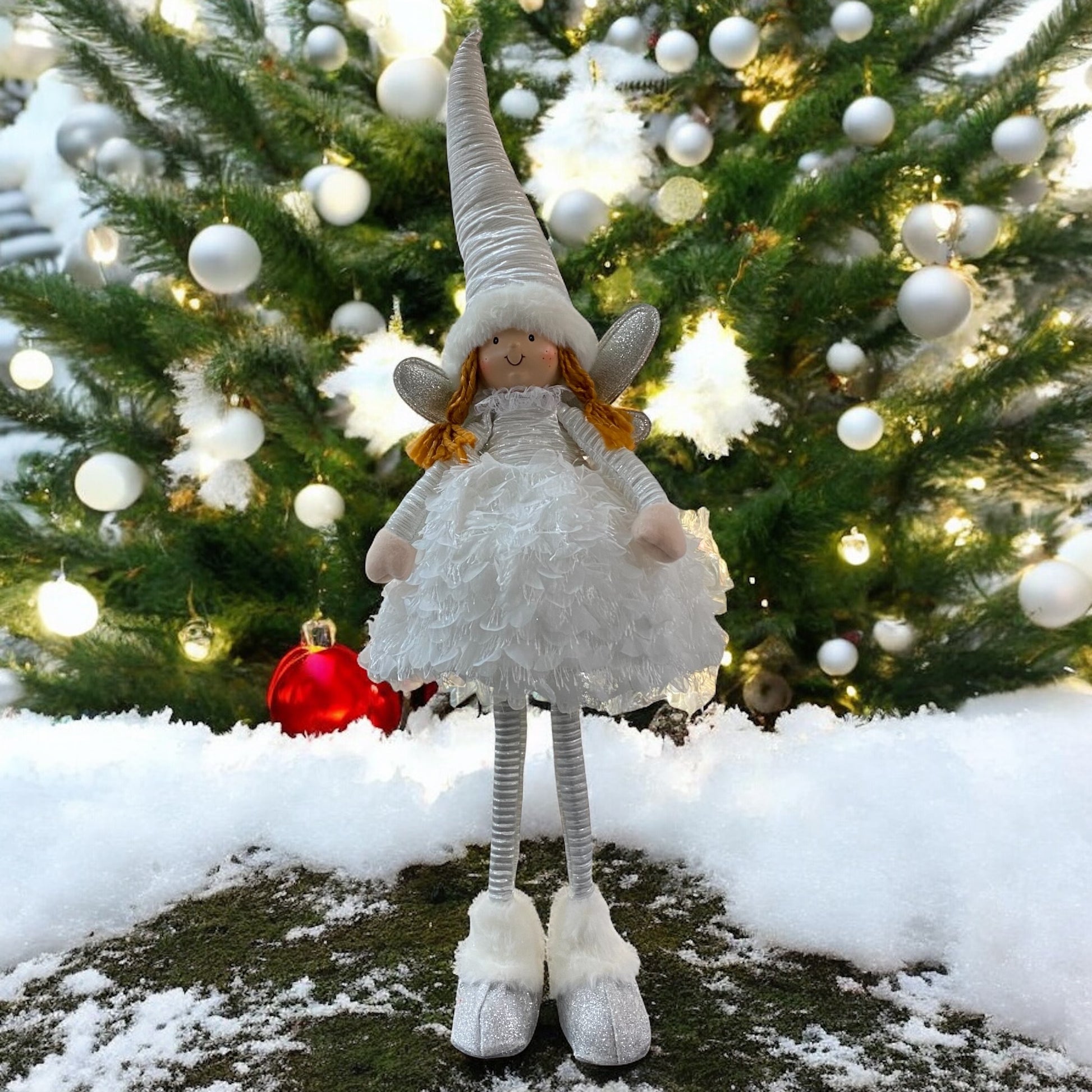 Eine stehende Stoff-Engelfigur mit langen Beinen, Zipfelmützen und flauschigem Kleid in Weiß im Ambiente