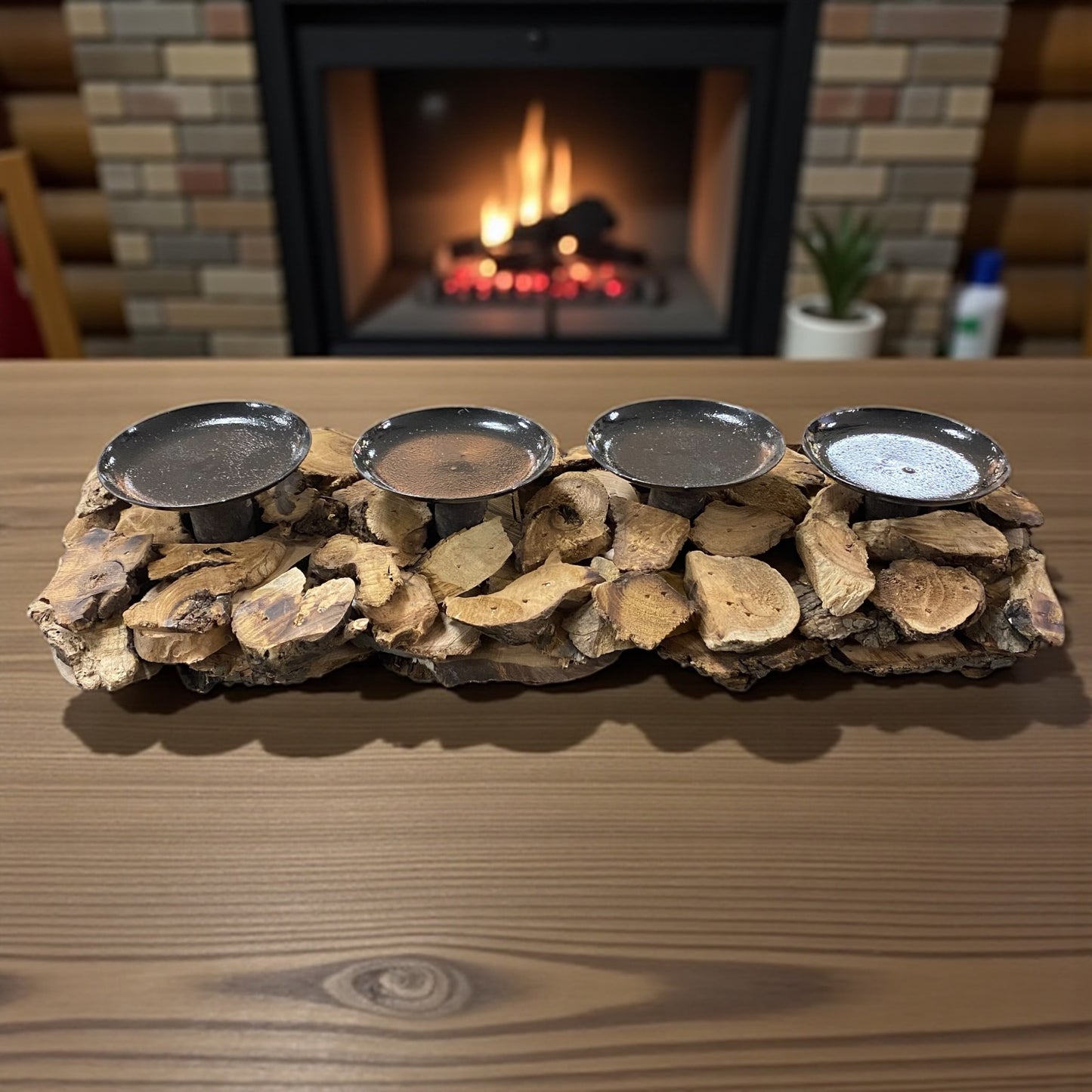 Rustikaler Holz-Adventskranz mit vier Metallkerzenhaltern, dekorativ auf einem Tisch vor Kaminfeuer platziert.