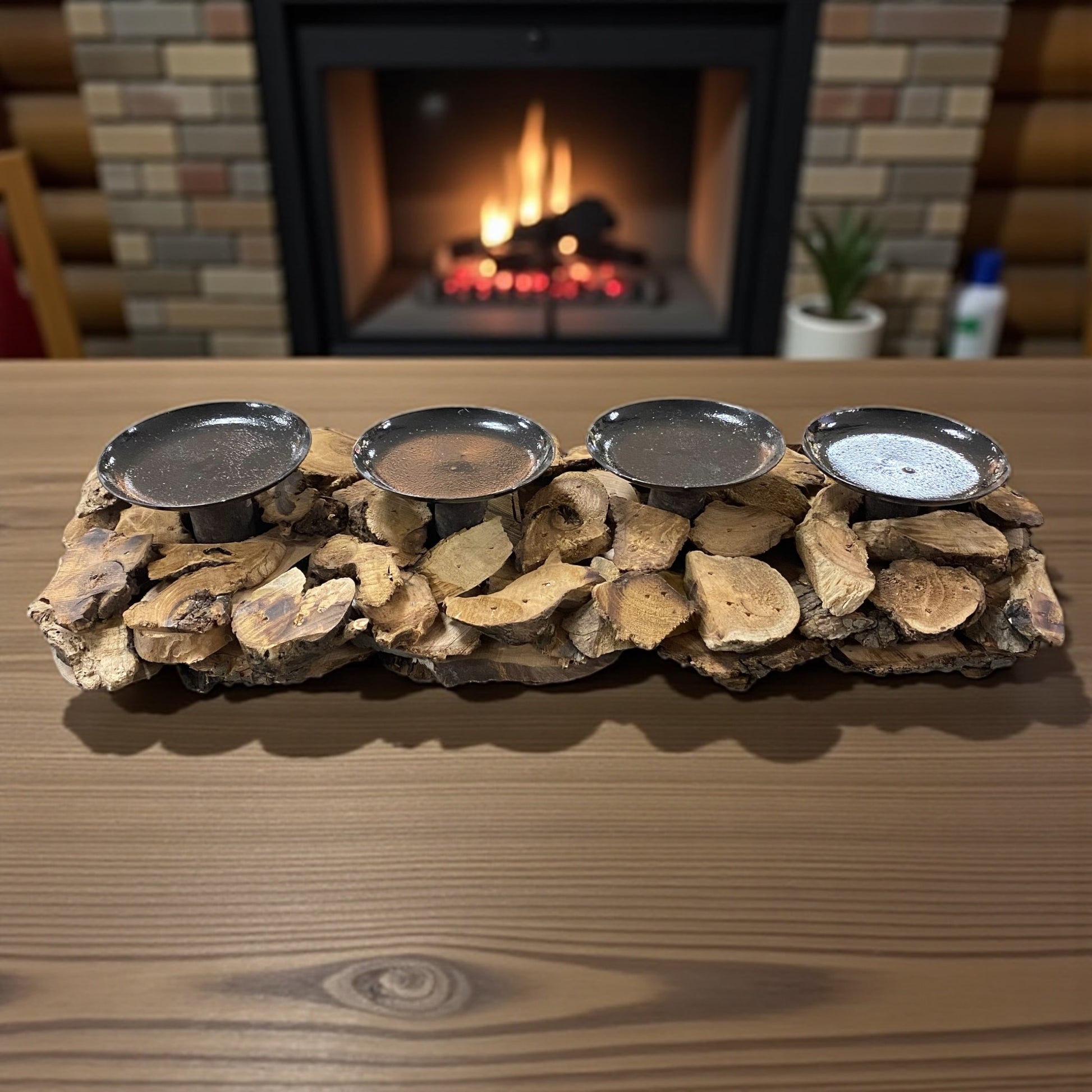 Rustikaler Holz-Adventskranz mit vier Metallkerzenhaltern, dekorativ auf einem Tisch vor Kaminfeuer platziert.