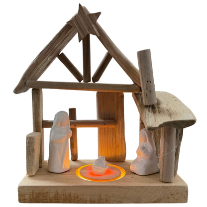 Holzkrippe in einfacher, offener Bauweise mit Dach und Stern an der Spitze. Im Inneren befinden sich drei weiße Keramikfiguren sowie eine kleine Figur in der Mitte. In die Basis ist eine runde LED-Beleuchtung integriert, freigestellt vor hellem Hintergrund.