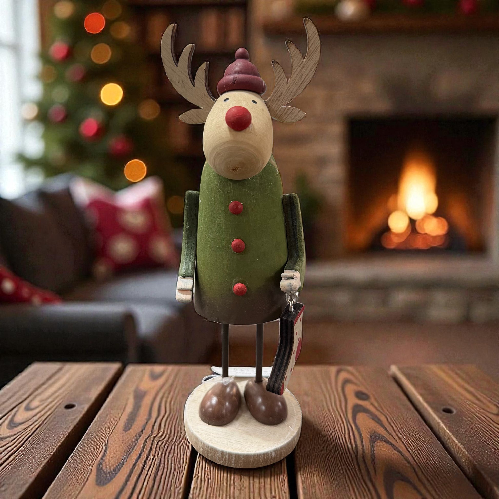 Eine dekorative Holz-Elchfigur mit Geweih und winterlicher Mütze steht stimmungsvoll vor einem Kamin.