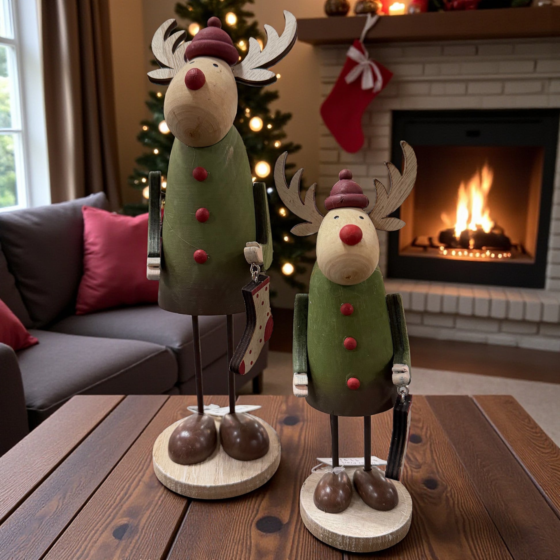 Zwei Holz-Elche in verschiedenen Größen stehen gemeinsam auf einem Tisch vor einem Kamin und sorgen für eine gemütliche Weihnachtsatmosphäre.
