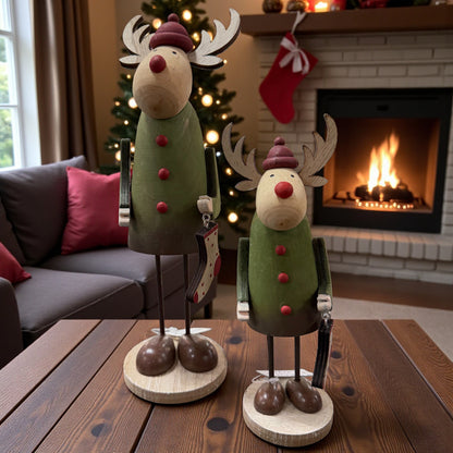 Zwei Holz-Elche in verschiedenen Größen stehen gemeinsam auf einem Tisch vor einem Kamin und sorgen für eine gemütliche Weihnachtsatmosphäre.
