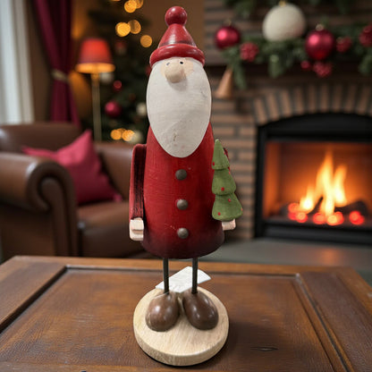 Eine einzelne Nikolausfigur aus Holz mit roter Kleidung und kleinem Tannenbaum wird stimmungsvoll vor einem Kamin präsentiert.
