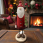 Eine einzelne Nikolausfigur aus Holz mit roter Kleidung und kleinem Tannenbaum wird stimmungsvoll vor einem Kamin präsentiert.