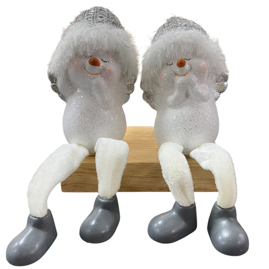 Zwei sitzende Schneemannfiguren mit grauen Mützen, weißen Beinen und grauen Schuhen auf einem Holzblock.