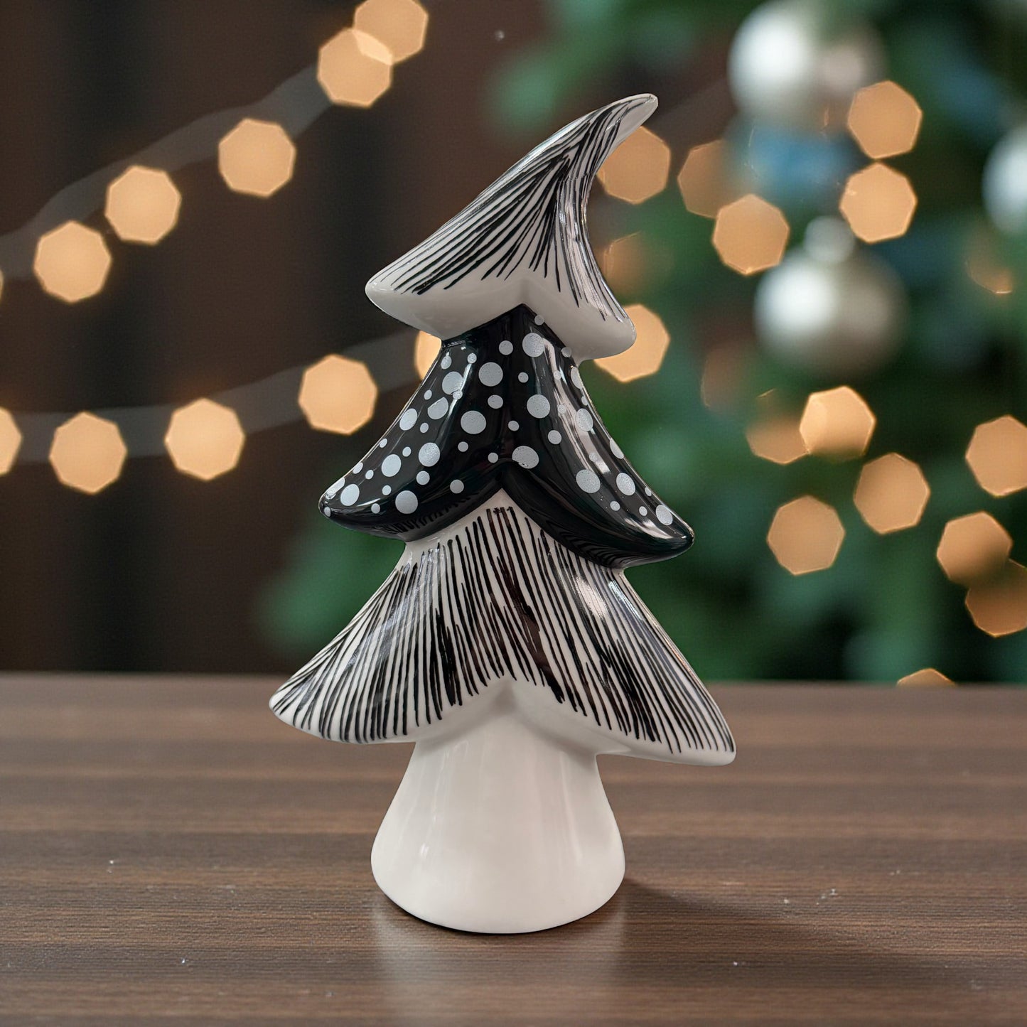 Ein schwarz-weiß gemusterter Keramik-Tannenbaum mit Punkt- und Linienstruktur steht auf einem Tisch vor einem festlich beleuchteten Hintergrund.