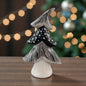 Ein schwarz-weiß gemusterter Keramik-Tannenbaum mit Punkt- und Linienstruktur steht auf einem Tisch vor einem festlich beleuchteten Hintergrund.