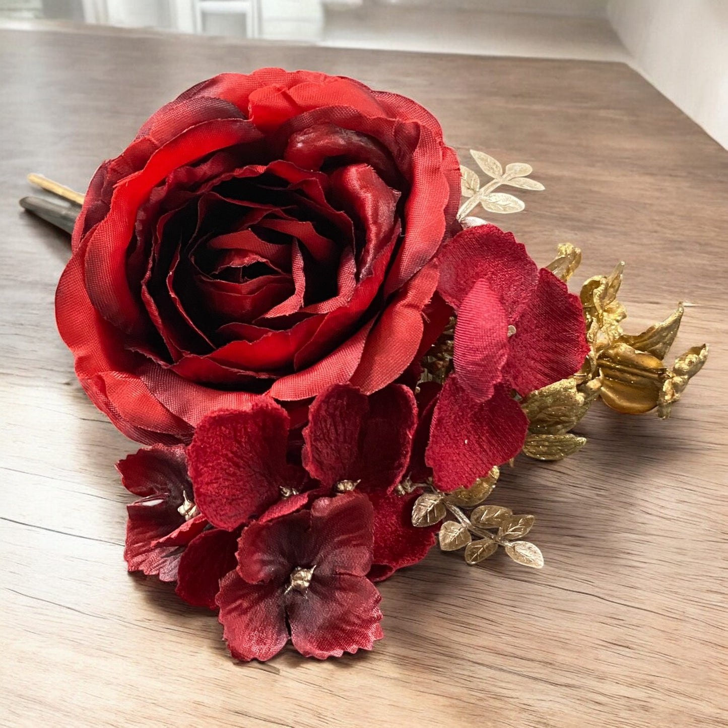 Kunstblume Rose in Rot mit goldenen Akzenten, festliche Deko auf Holztisch arrangiert.