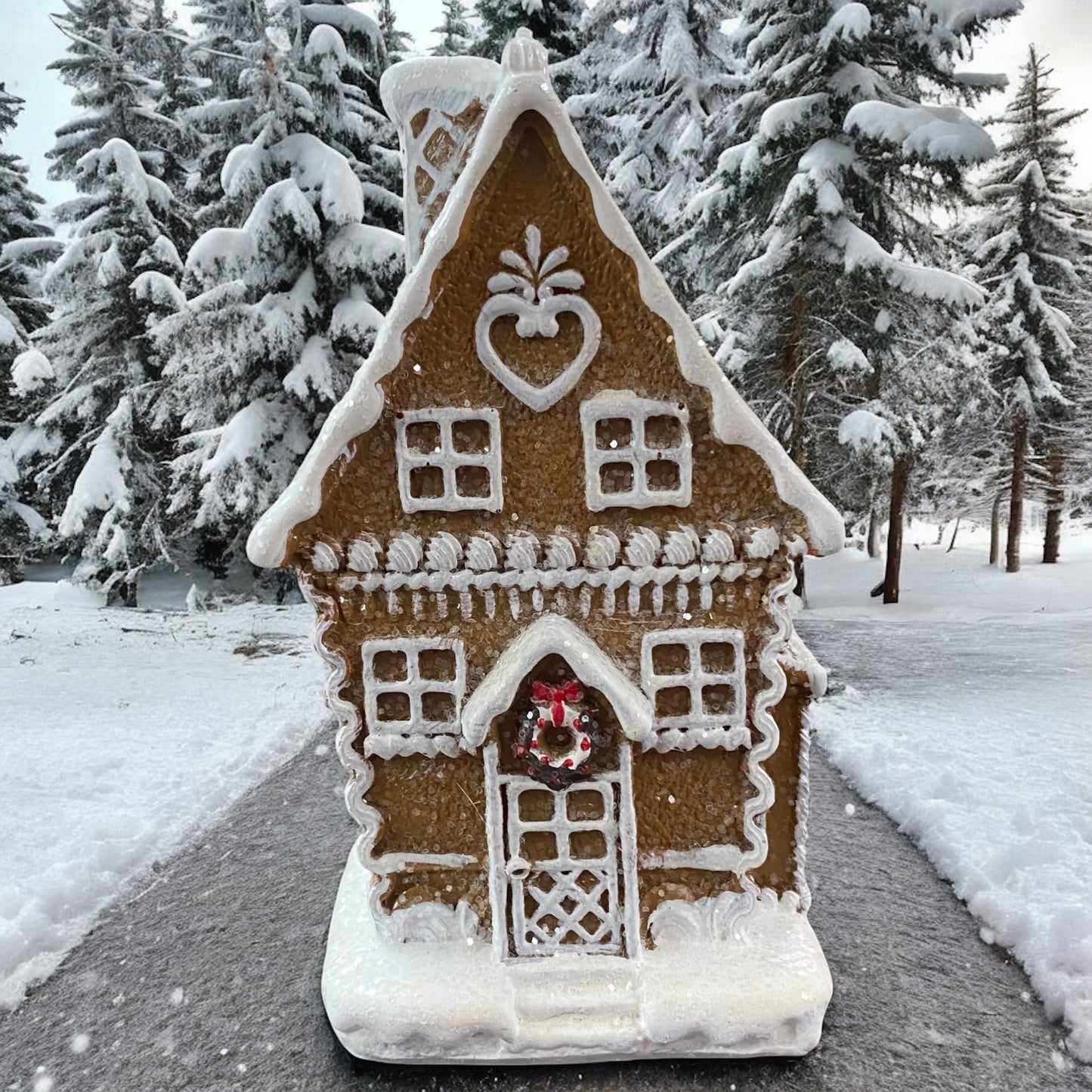 Weihnachtliches Lebkuchenhaus von Formano mit warmem Licht, verschneite Tannen im Hintergrund.