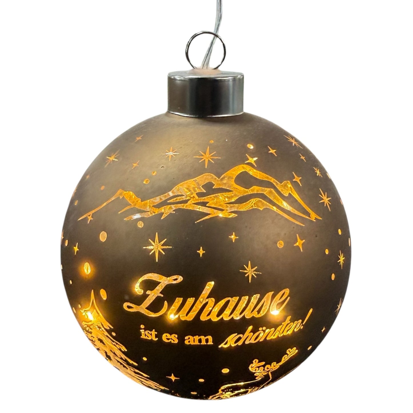 Eine runde, braune LED-Dekokugel zum Aufhängen mit warmweißem Licht zeigt eine winterliche Szene mit Bergen, Tannenbaum, Hirsch und dem Schriftzug „Zuhause ist es am schönsten!“.
