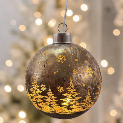 Dunkle Kugel mit winterlichem Waldmotiv und warmem Licht im Inneren hängt dekorativ im Raum.