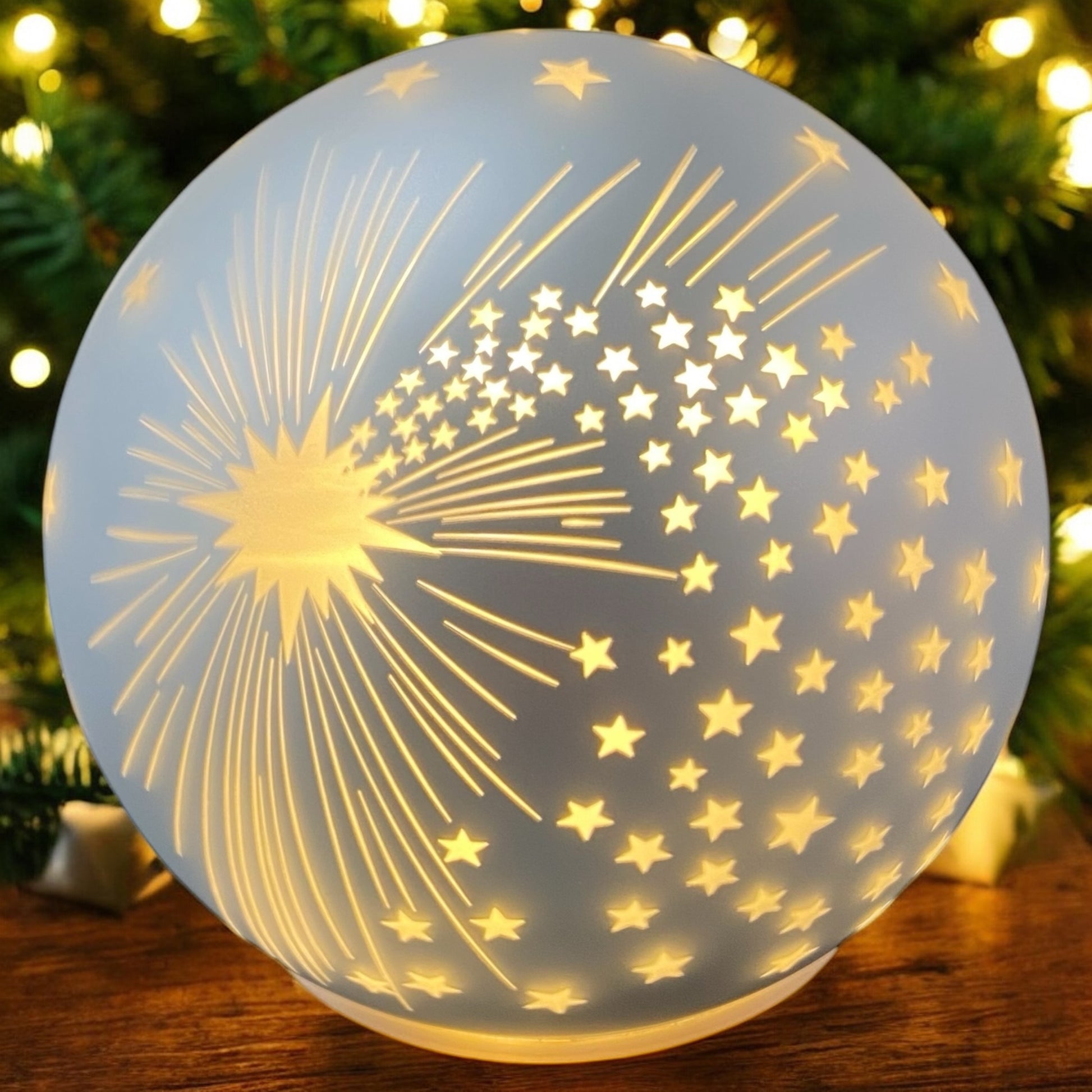 Runde LED-Deko-Kugel in mattem Silber mit ausgestanztem Sternenmotiv und leuchtendem Sternenmuster vor weihnachtlichem Ambiente