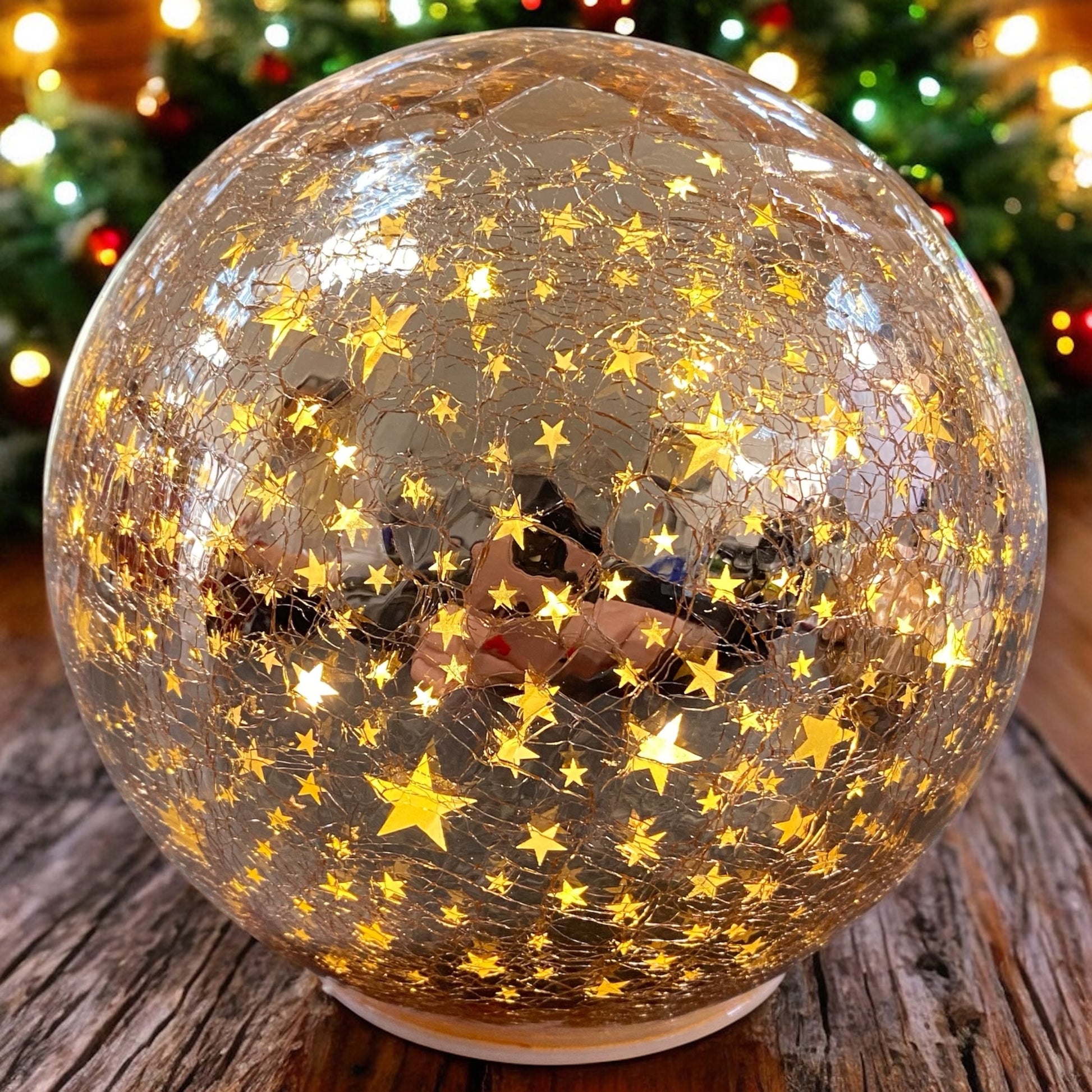 Leuchtende rosa Crackle-Glas-Kugel mit goldenen Sternenmotiven, strahlend im warmen Licht eines weihnachtlichen Ambientes.