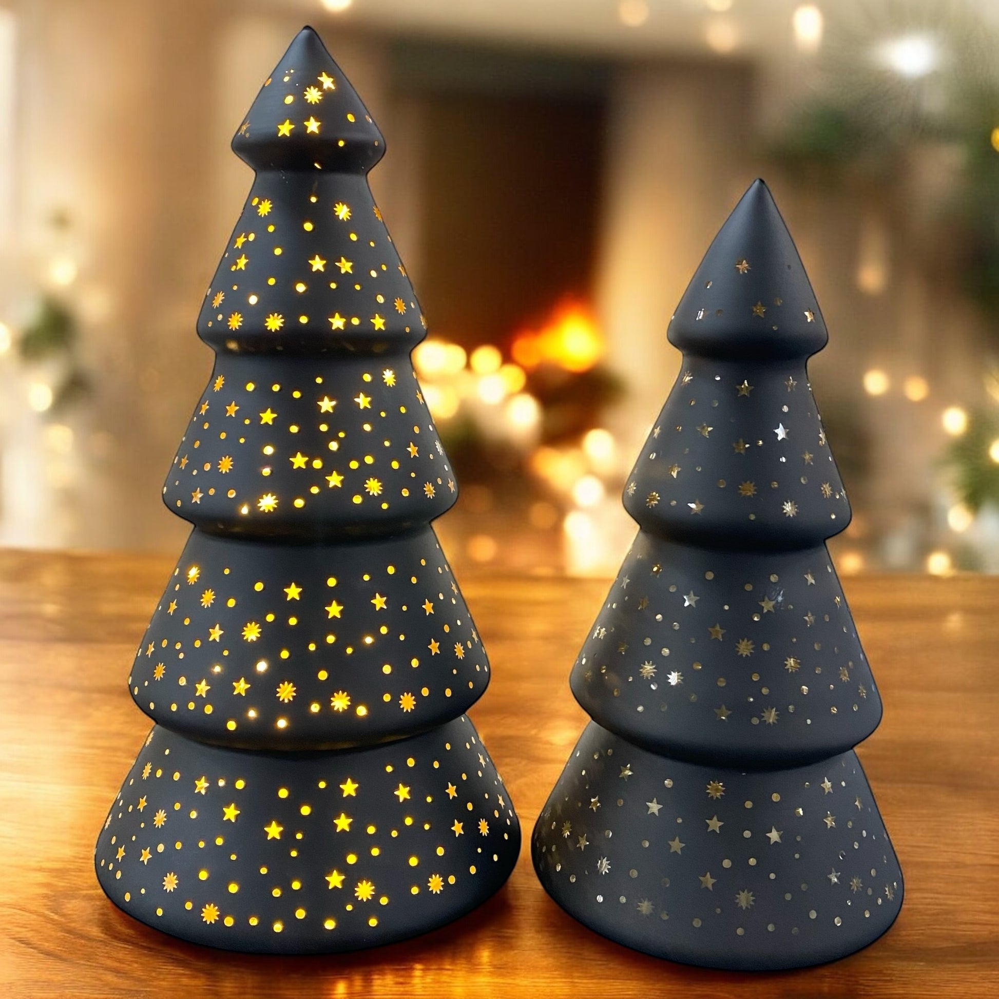 Leuchtende schwarze Deko-Tannenbäume mit Sternenmuster, stimmungsvoll auf einem Holztisch vor warmem Hintergrund arrangiert.