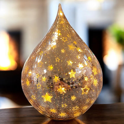 Ein rosa LED-Deko-Tropfen aus Crackle-Glas mit goldenen Sternen, strahlend im warmen Licht eines festlichen Ambientes.