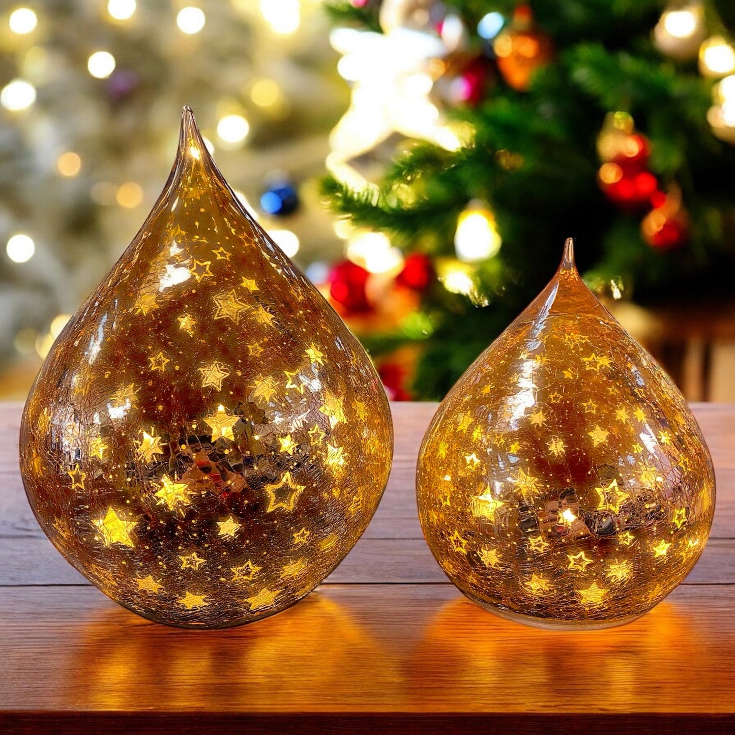 Leuchtende rosa Crackle-Glas-Tropfen mit goldenen Sternen auf Holztisch vor funkelndem Lichterhintergrund.