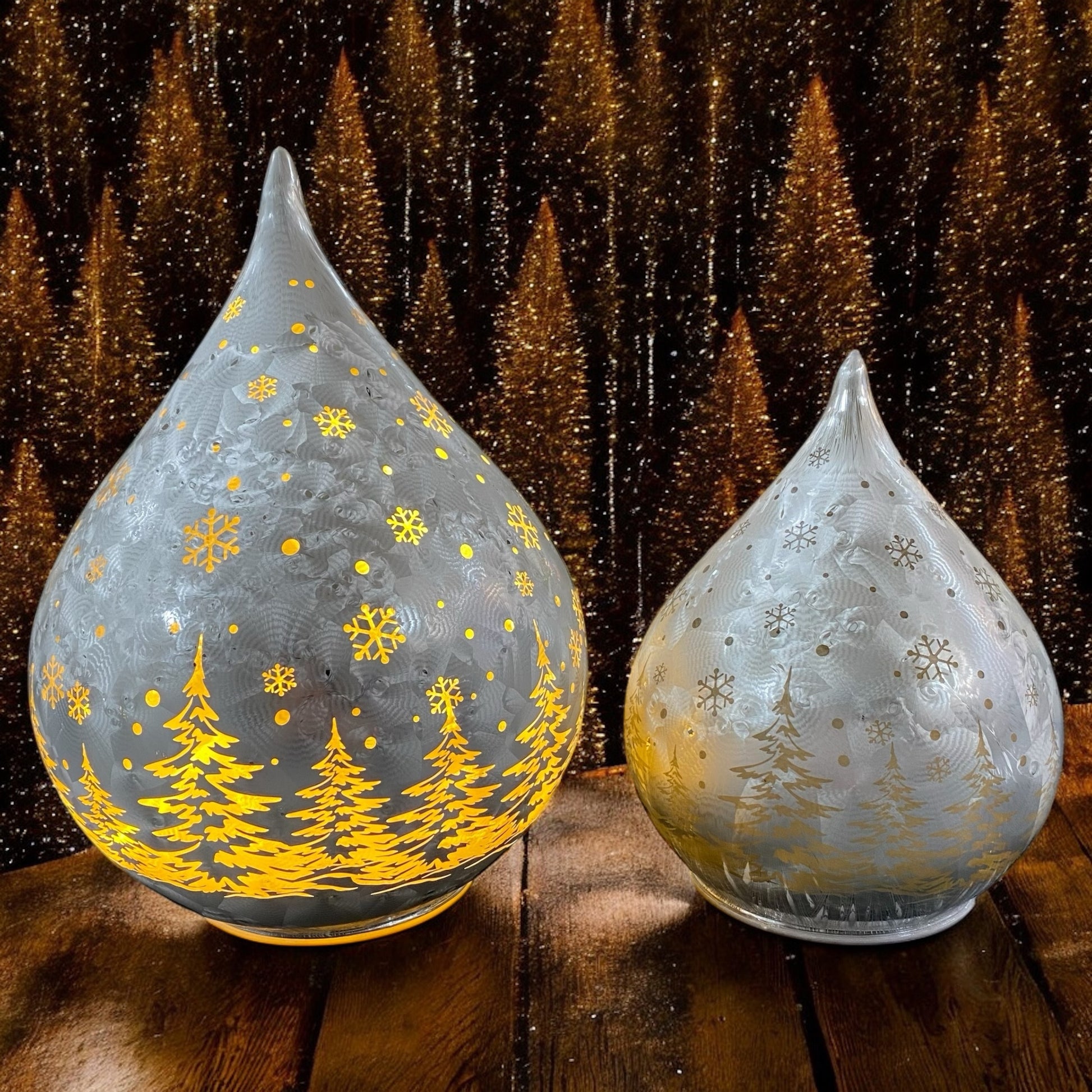 Leuchtende silberne Deko-Tropfen mit goldener Winterlandschaft auf Holztisch vor glitzerndem Hintergrund.