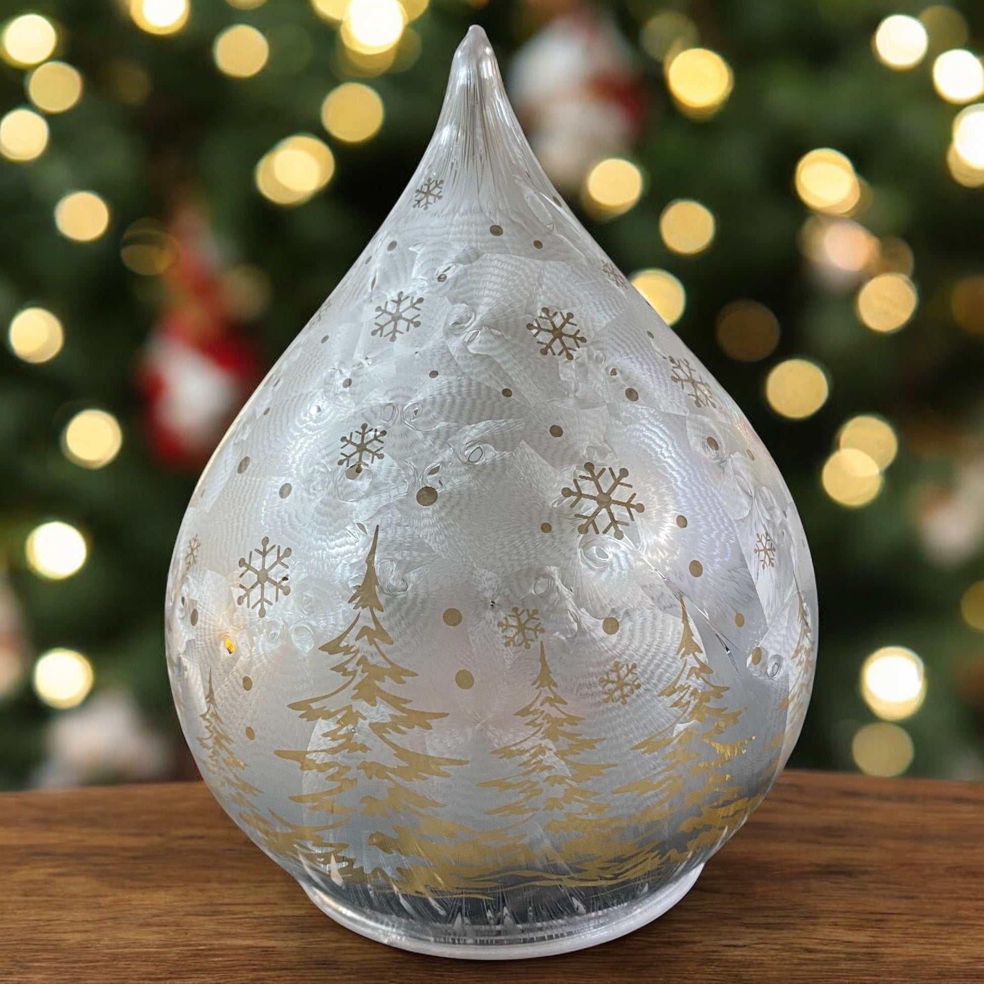 Silberner Deko-Tropfen mit goldenen Tannenbäumen und Schneeflockenmotiv, unbeleuchtet vor weihnachtlicher Kulisse.