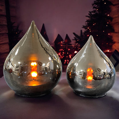 Zwei silberne LED-Deko-Tropfen mit warm leuchtender Flamme, stimmungsvoll in winterlicher Umgebung präsentiert.