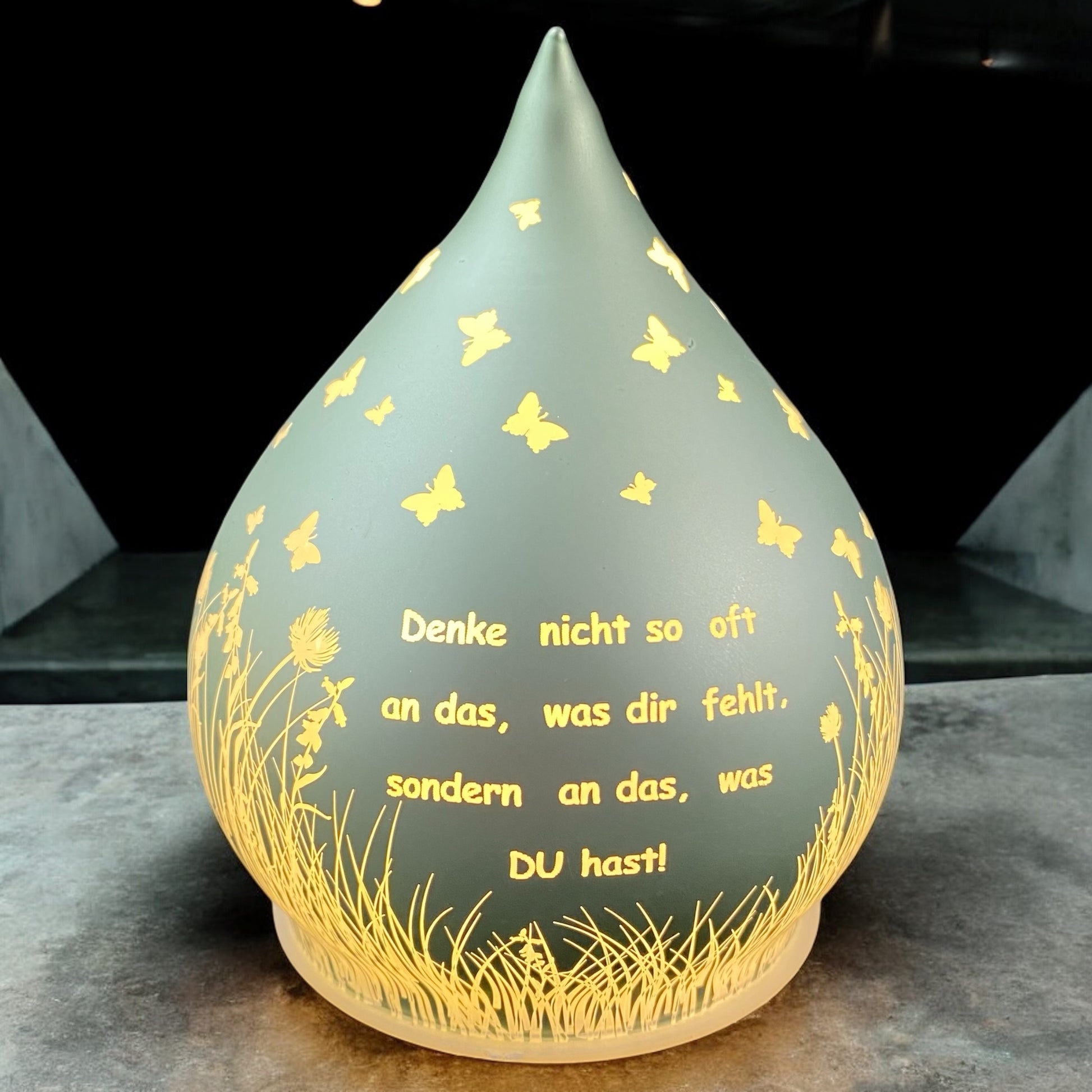 Mintgrünes Dekolicht in Tropfenform mit Spruch „Denke nicht so oft an das, was dir fehlt, sondern an das, was du hast!“ im Ambiente