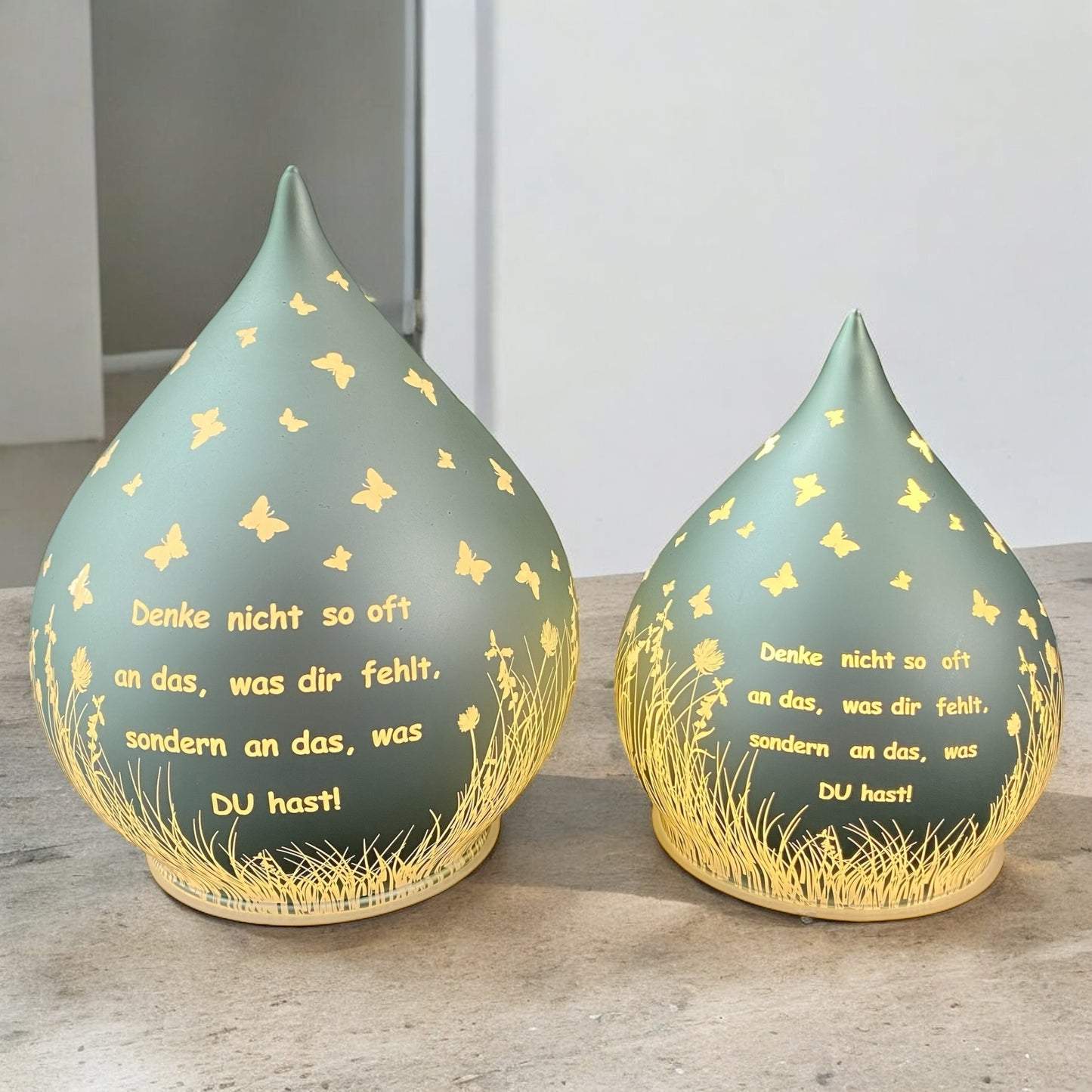 Zwei Mintgrüne Dekolichter in Tropfenform mit Spruch „Denke nicht so oft an das, was dir fehlt, sondern an das, was du hast!“ in zwei Größen im Ambiente