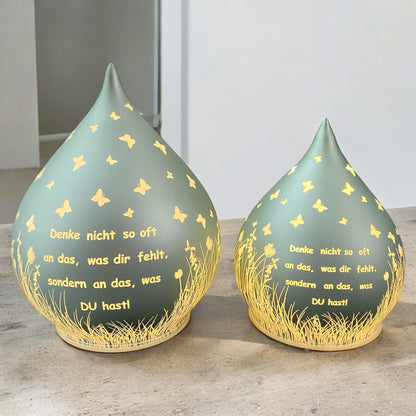 Zwei Mintgrüne Dekolichter in Tropfenform mit Spruch „Denke nicht so oft an das, was dir fehlt, sondern an das, was du hast!“ in zwei Größen im Ambiente