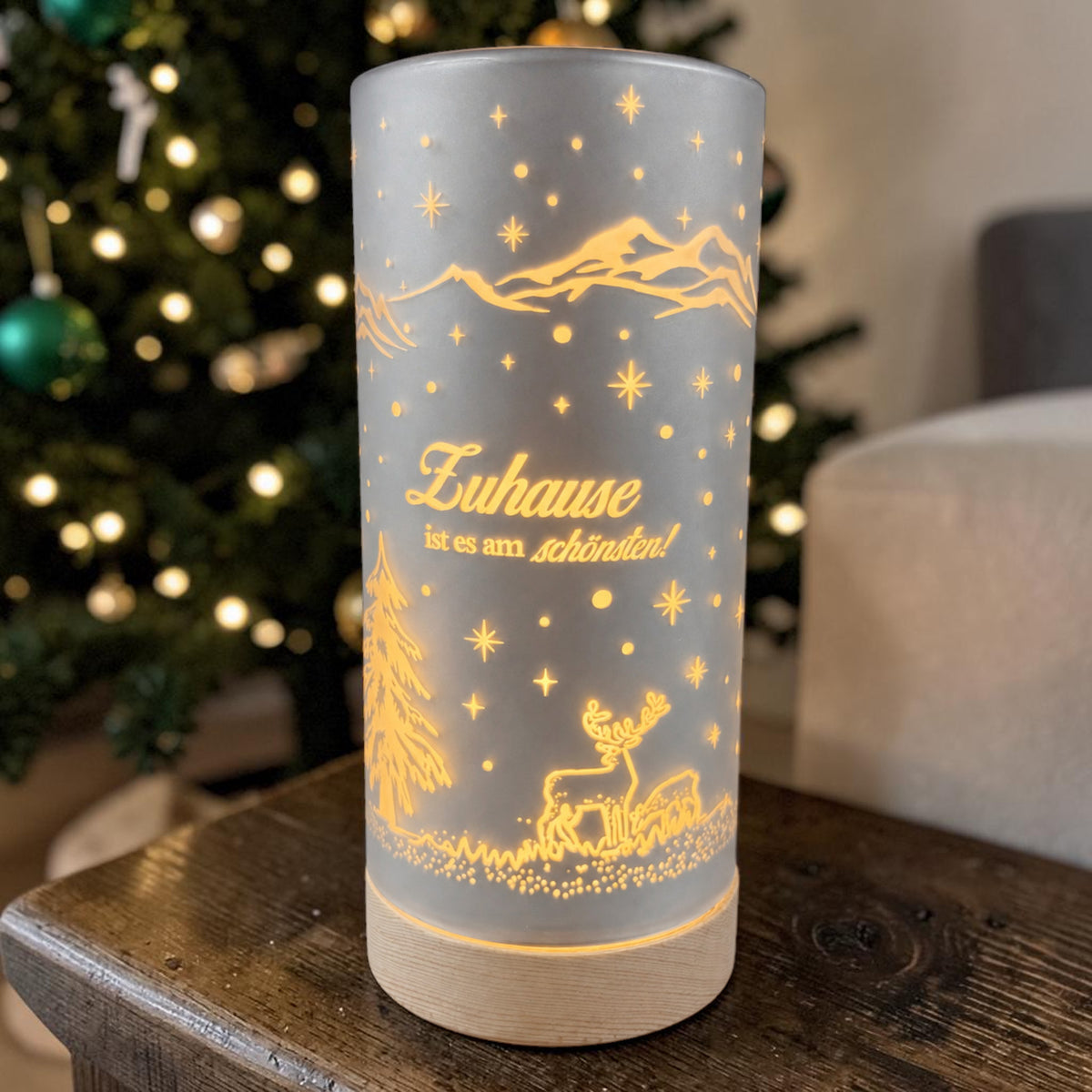Große silberne Formano LED Säule „Zuhause ist es am schönsten!“ mit Holzsockel und warm leuchtendem Wintermotiv vor einem Weihnachtsbaum.