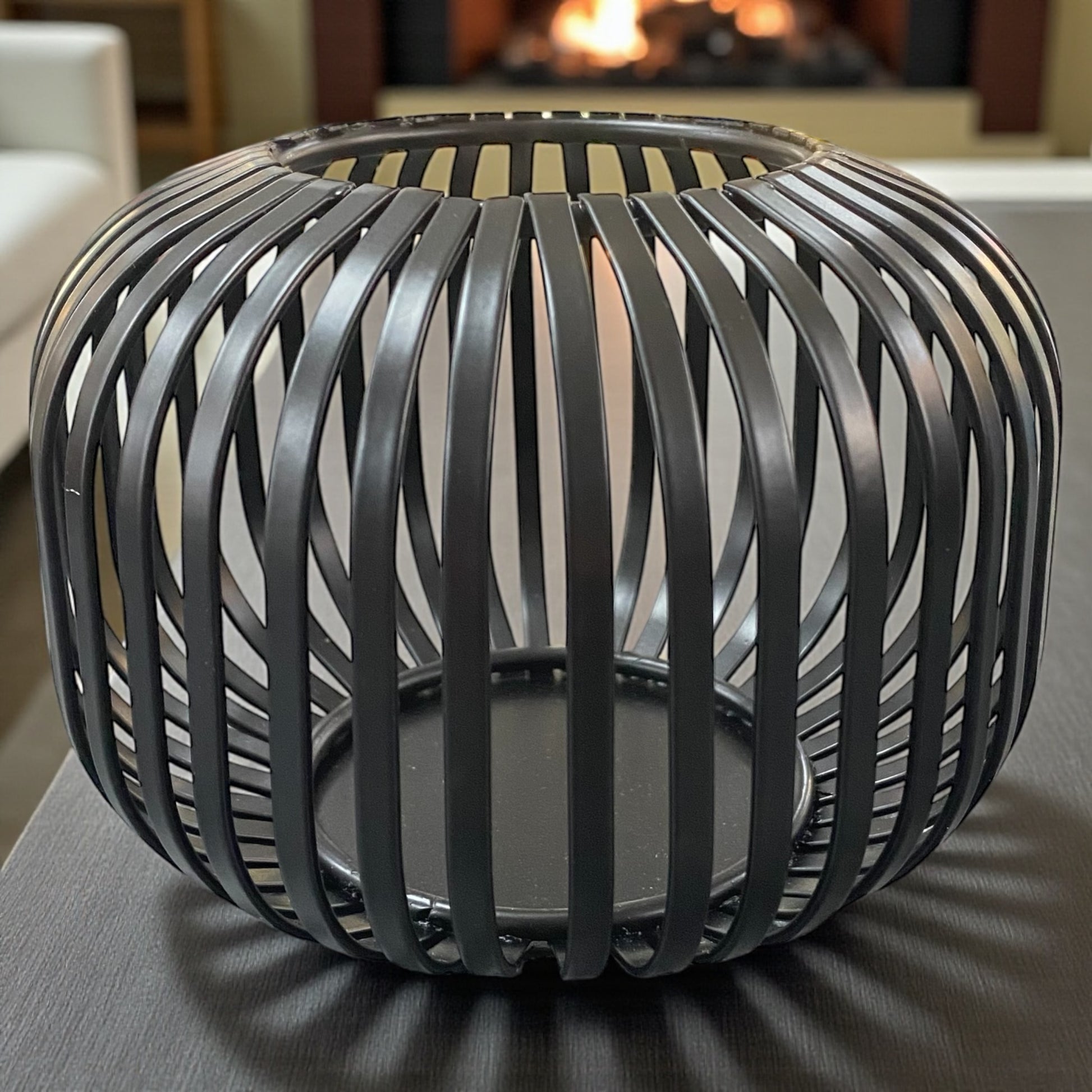 Kleines Formano Windlicht aus schwarzem Metall mit dekorativer Strebenoptik, auf Tisch vor Kamin platziert.