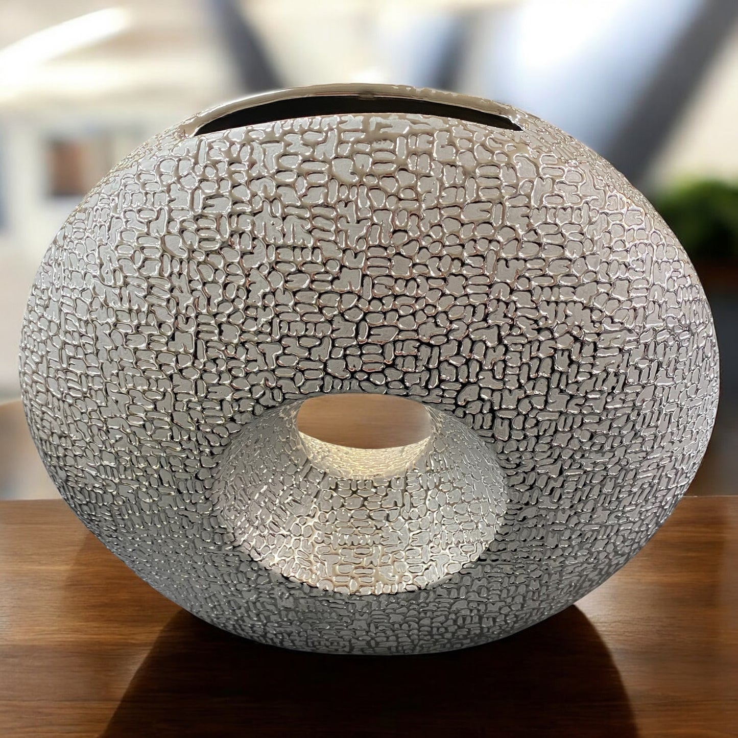 Formano silberne Deko-Vase mit runder Öffnung und strukturierter Oberfläche, stilvoll auf Holztisch arrangiert.